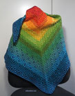 A triengular, crocheted shawl, with geometric patterns in a gradient from red in the centre to blue at the edges, draped over the back of an office chair.
